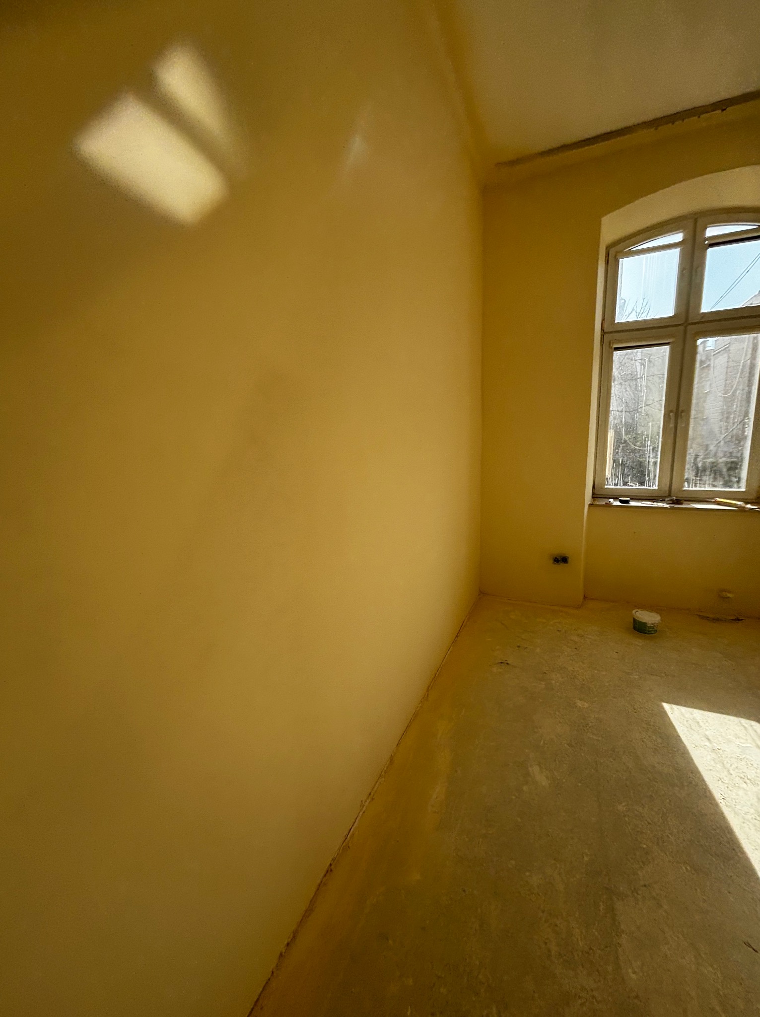 Pokój po remoncie: gładkie, żółte ściany, okno z widokiem na drzewa, przygotowana podłoga. Świeże wykończenie, gotowe do dalszych prac.