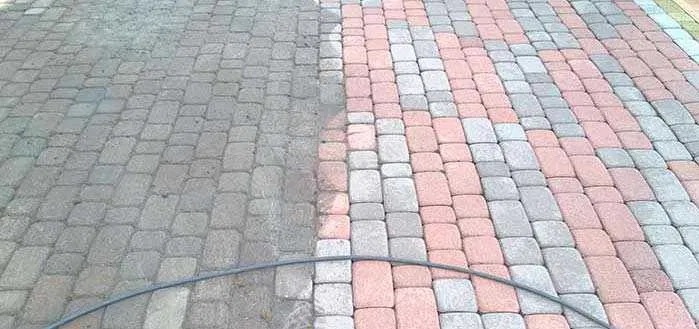 Mycie kostki brukowej: Widoczna różnica między brudną (szarą) a czystą (różowo-szarą) częścią kostki, z przewodem od myjki ciśnieniowej leżącym na kostce.