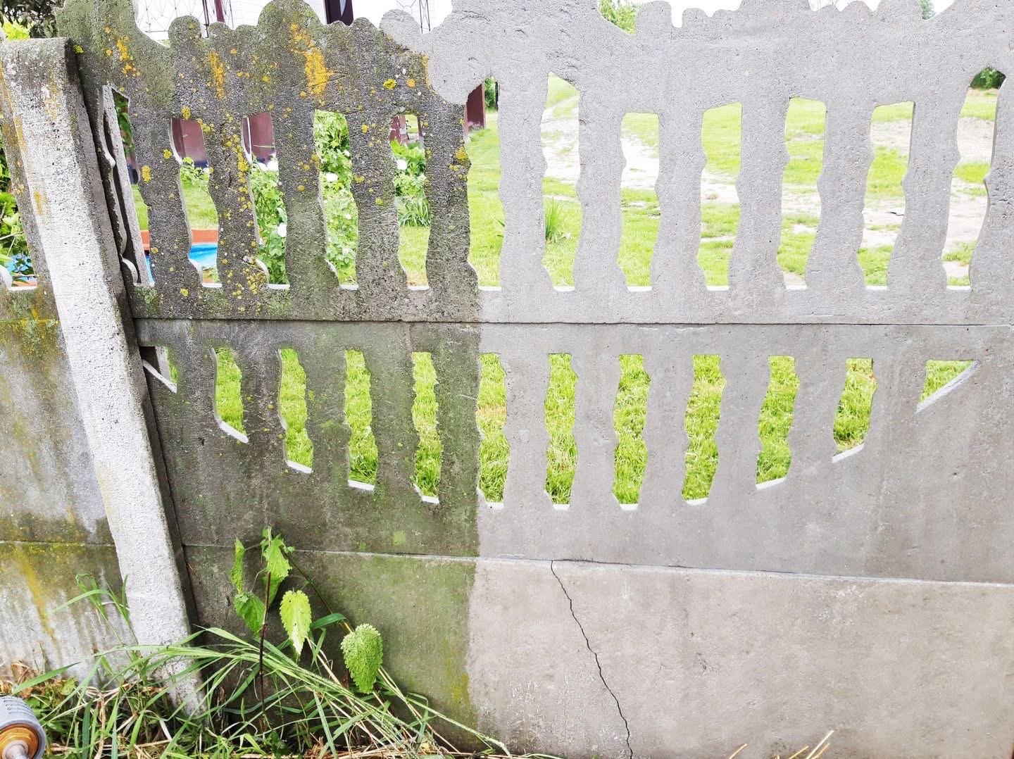 Betonowy ażurowy płot, czyszczony do połowy, z widoczną różnicą między brudną, porośniętą mchem częścią a czystą powierzchnią, z zielenią w tle.