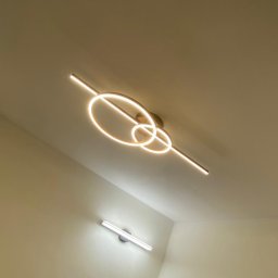 ElektroSync - Nowoczesna lampa sufitowa LED z geometrycznym wzorem, świecąca ciepłym światłem. Widoczna również listwa LED na ścianie. Ujęcie z dołu, podkreślające design oświetlenia.