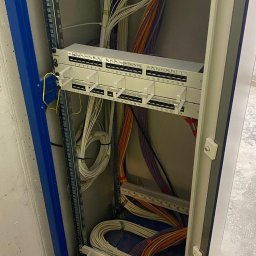 ElektroSync - Rozdzielnica elektryczna w szafie z uporządkowanymi kablami o różnych kolorach, zakończonymi złączami. Widoczne numery identyfikacyjne na panelach.