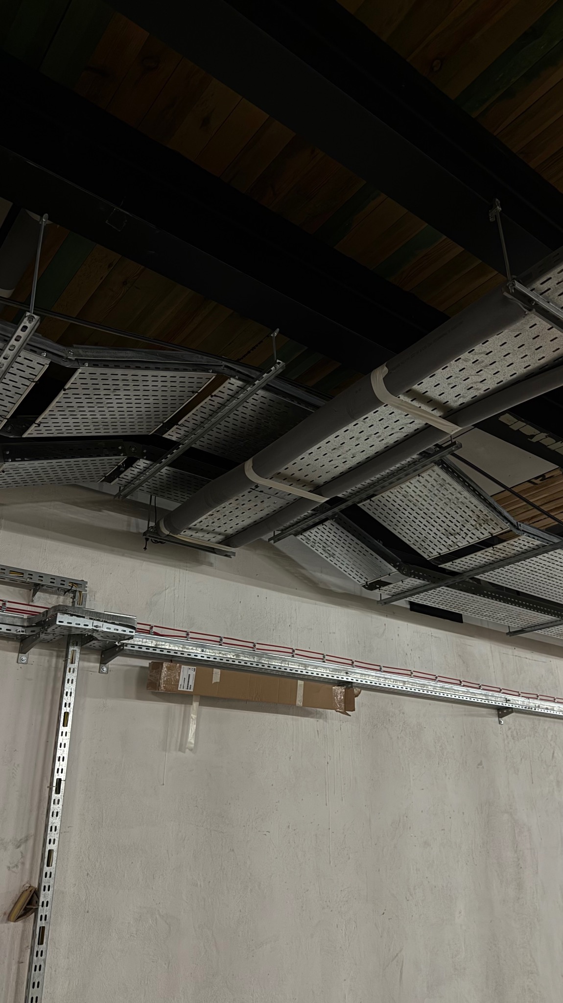 Sufit z widocznymi instalacjami elektrycznymi: koryta kablowe z przewodami, rury. Elementy konstrukcyjne pomalowane na czarno, drewniane deski sufitowe.