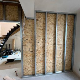 ReNovoPro Oleksandr Shevchenko - Stelaż z profili stalowych wypełniony płytą OSB, tworzący ściankę działową w trakcie remontu, widok na schody w tle.