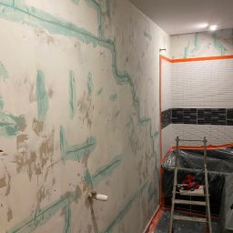 ReNovoPro Oleksandr Shevchenko - Przygotowanie ścian w łazience do położenia płytek, widoczne pionowe i poziome ślady po taśmie malarskiej zabezpieczającej instalacje, częściowo wykończone płytki na ścianie, drabina w tle...