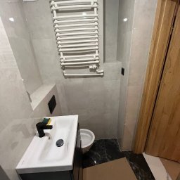 ReNovoPro Oleksandr Shevchenko - Wykończona łazienka w szarościach z czarnymi akcentami: biała umywalka z czarną armaturą, grzejnik drabinkowy i marmurowe płytki podłogowe, widoczny fragment drewnianych drzwi.