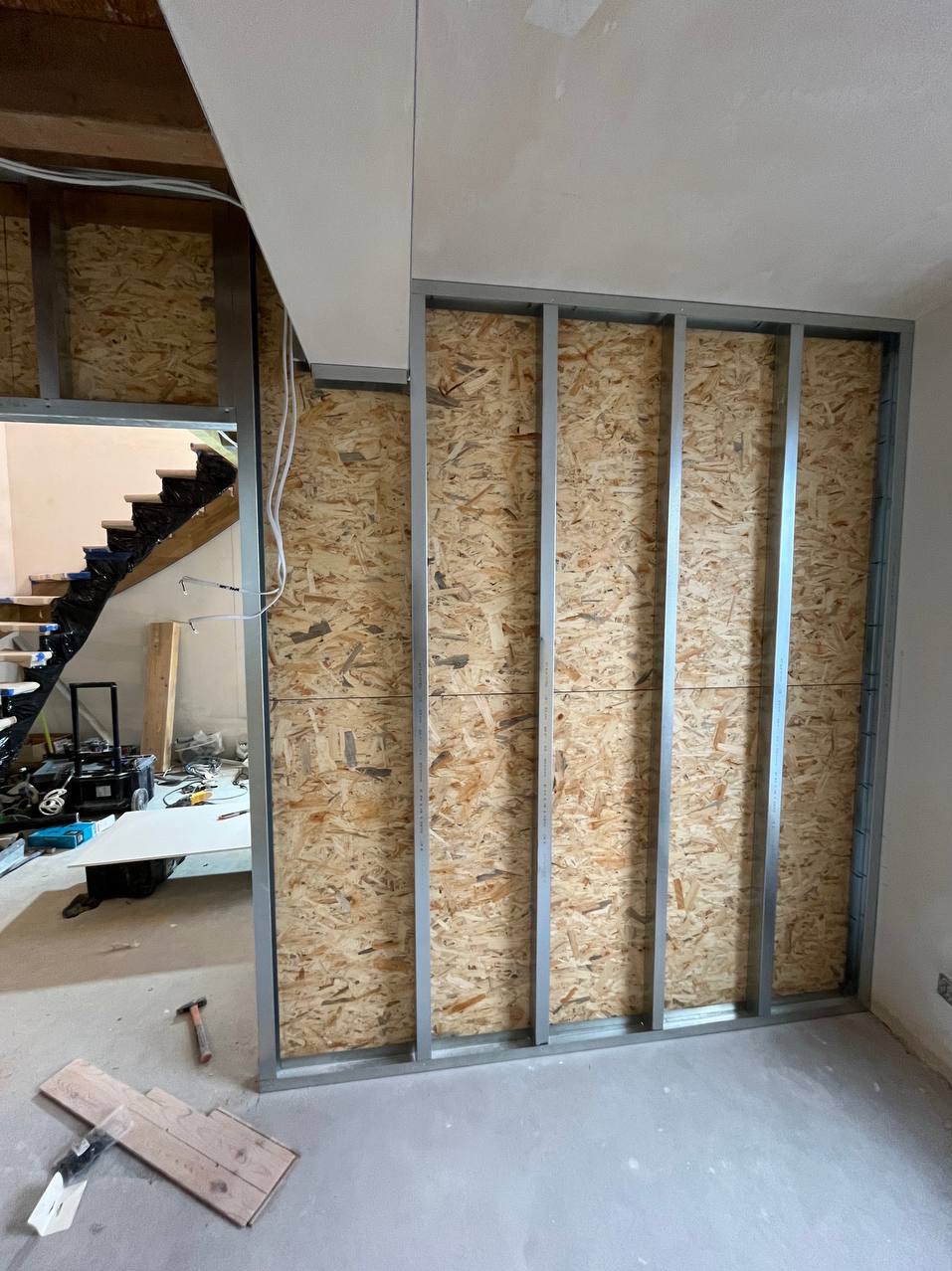 Stelaż z profili stalowych wypełniony płytą OSB, tworzący ściankę działową w trakcie remontu, widok na schody w tle.