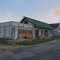 FRB ORAWIEC Wojciech Orawiec - Budowa parterowego budynku z betonu komórkowego w trakcie realizacji, z częściowo położonym zielonym dachem i zabezpieczeniami budowlanymi, widok z ulicy.