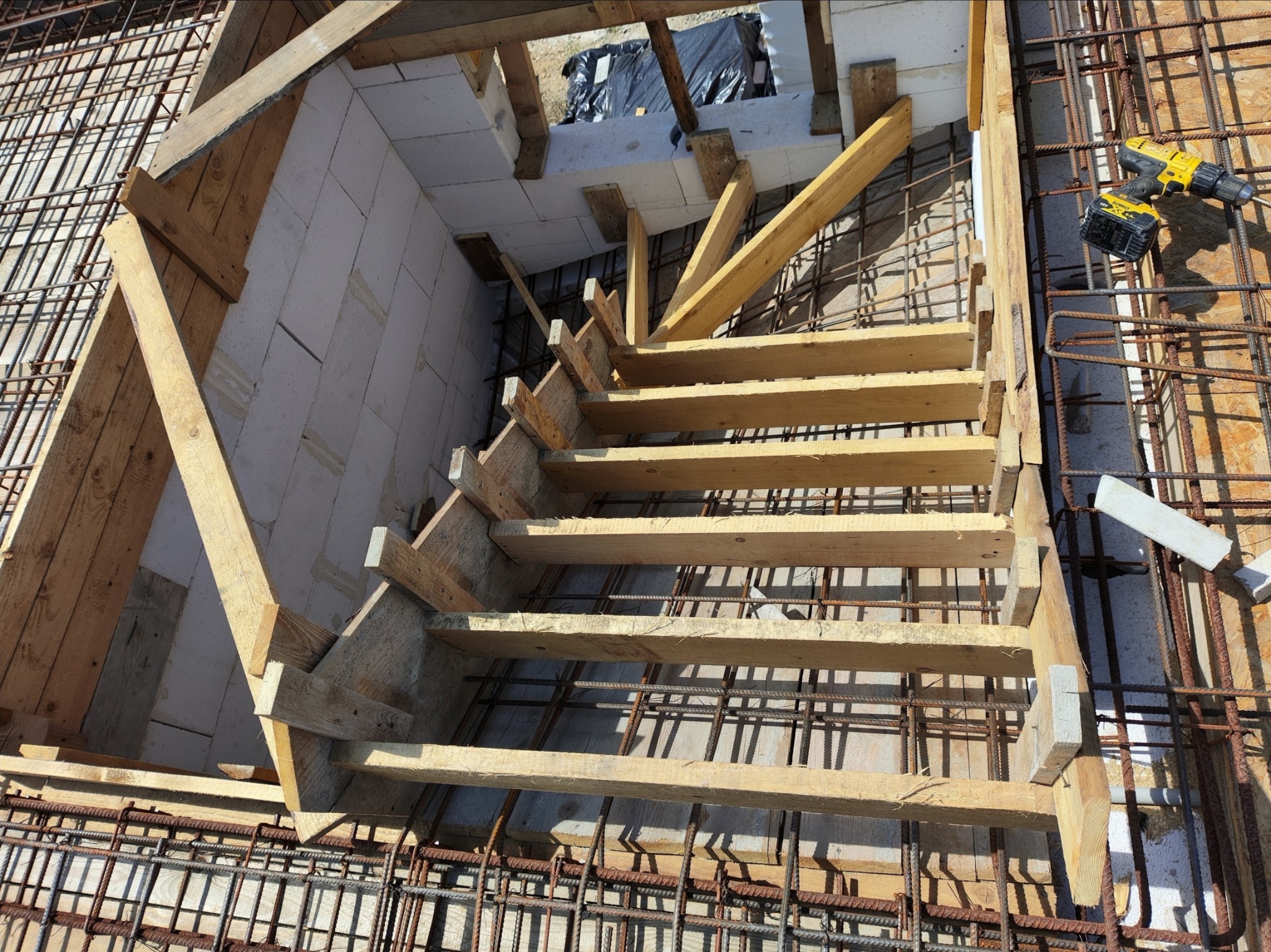 Zbrojenie fundamentu schodów z szalunkiem drewnianym i bloczkami betonowymi, widoczne narzędzia budowlane.