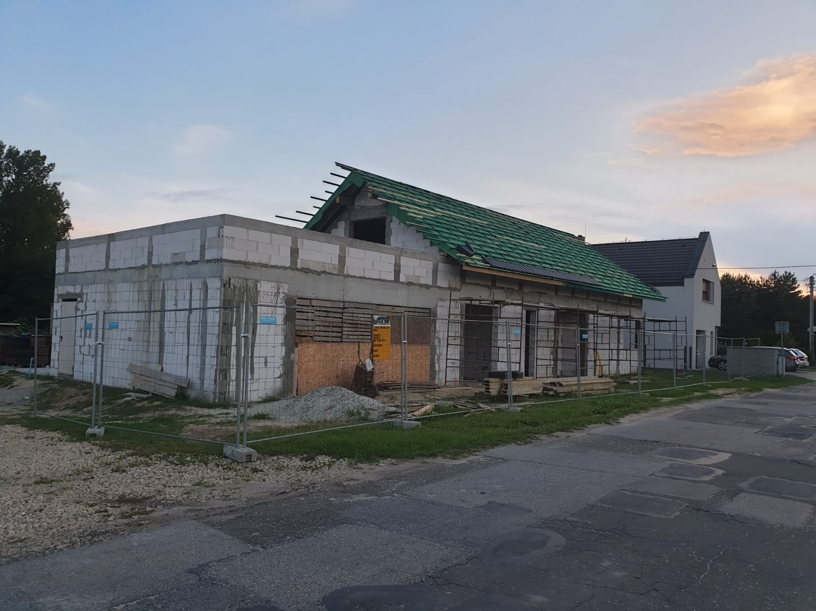 Budowa parterowego budynku z betonu komórkowego w trakcie realizacji, z częściowo położonym zielonym dachem i zabezpieczeniami budowlanymi, widok z ulicy.