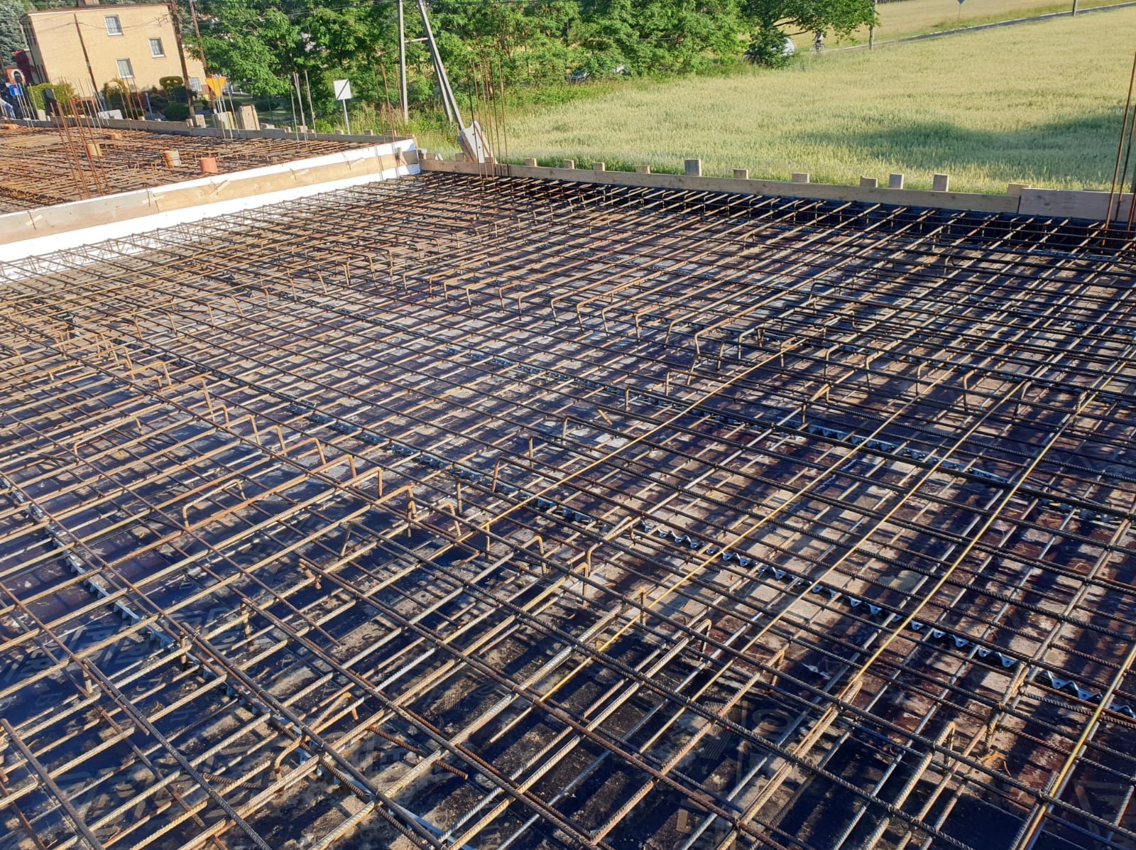 Siatka zbrojeniowa ułożona na czarnej folii, przygotowana do wylania fundamentów pod budynek, widok z góry.