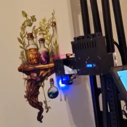 Drukarka ścienna w trakcie nanoszenia grafiki z motywem półki z eliksirami na jasną ścianę, widoczne dysze drukujące i niebieskie światło lasera pozycjonującego.