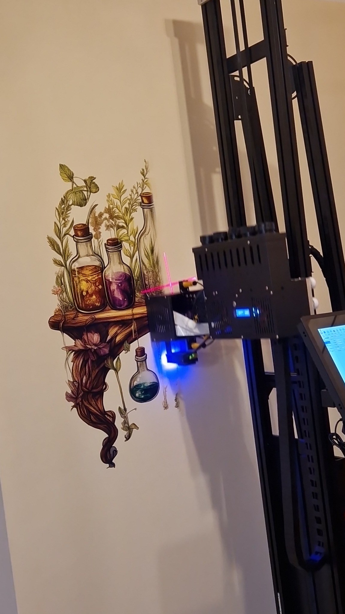 Drukarka ścienna w trakcie nanoszenia grafiki z motywem półki z eliksirami na jasną ścianę, widoczne dysze drukujące i niebieskie światło lasera pozycjonującego.