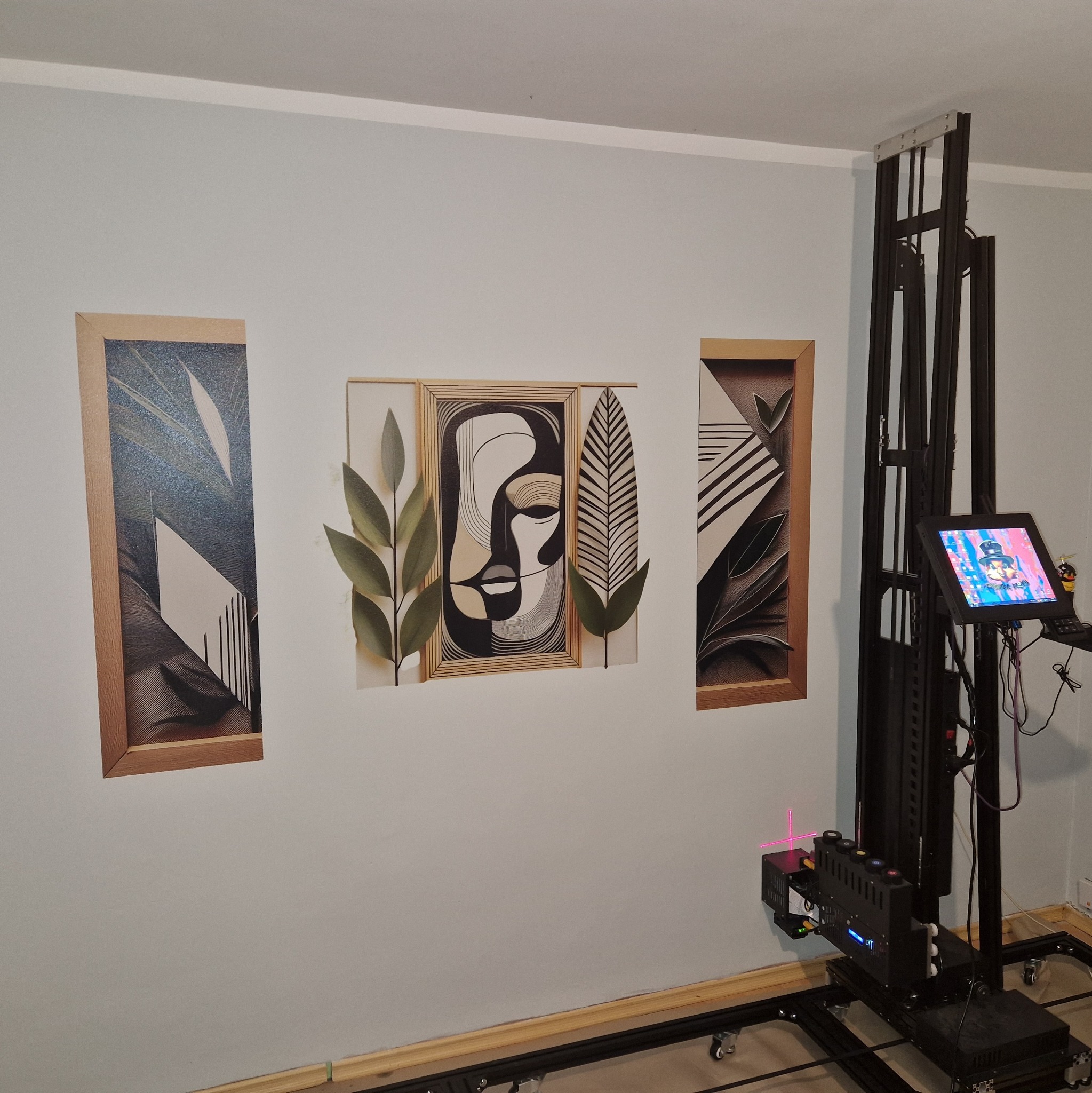 Ściana z trzema obrazami w drewnianych ramach, drukowanymi bezpośrednio na ścianie za pomocą mobilnej drukarki pionowej z laserowym systemem pozycjonowania.