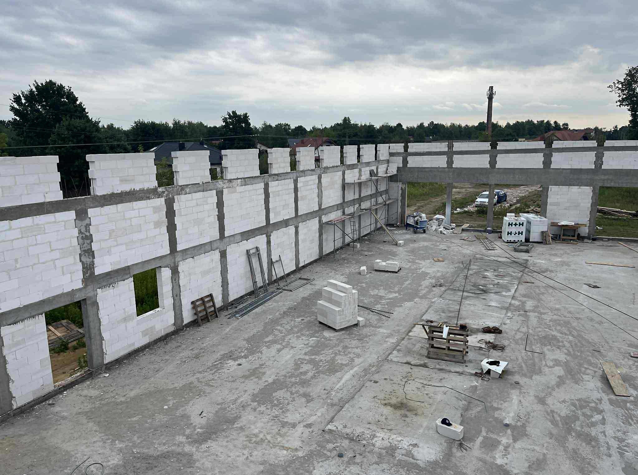 Budowa domu z betonu komórkowego: wznoszenie ścian parteru z widocznymi otworami okiennymi. Na pierwszym planie materiały budowlane i narzędzia.