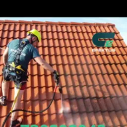 Pracownik w uprzęży, w kasku ochronnym, czyści dach z czerwonej dachówki za pomocą myjki ciśnieniowej; widoczny efekt czyszczenia, logo firmy w prawym górnym rogu i numer telefonu nałożony na obraz.