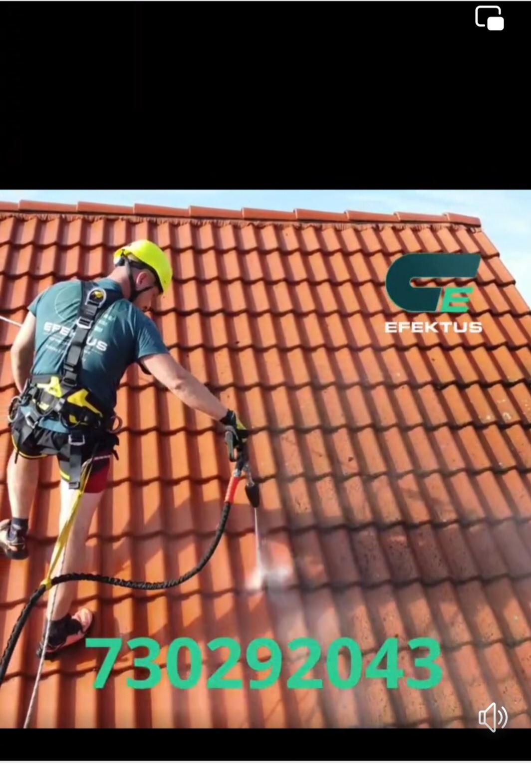 Pracownik w uprzęży, w kasku ochronnym, czyści dach z czerwonej dachówki za pomocą myjki ciśnieniowej; widoczny efekt czyszczenia, logo firmy w prawym górnym rogu i numer telefonu nałożony na obraz.