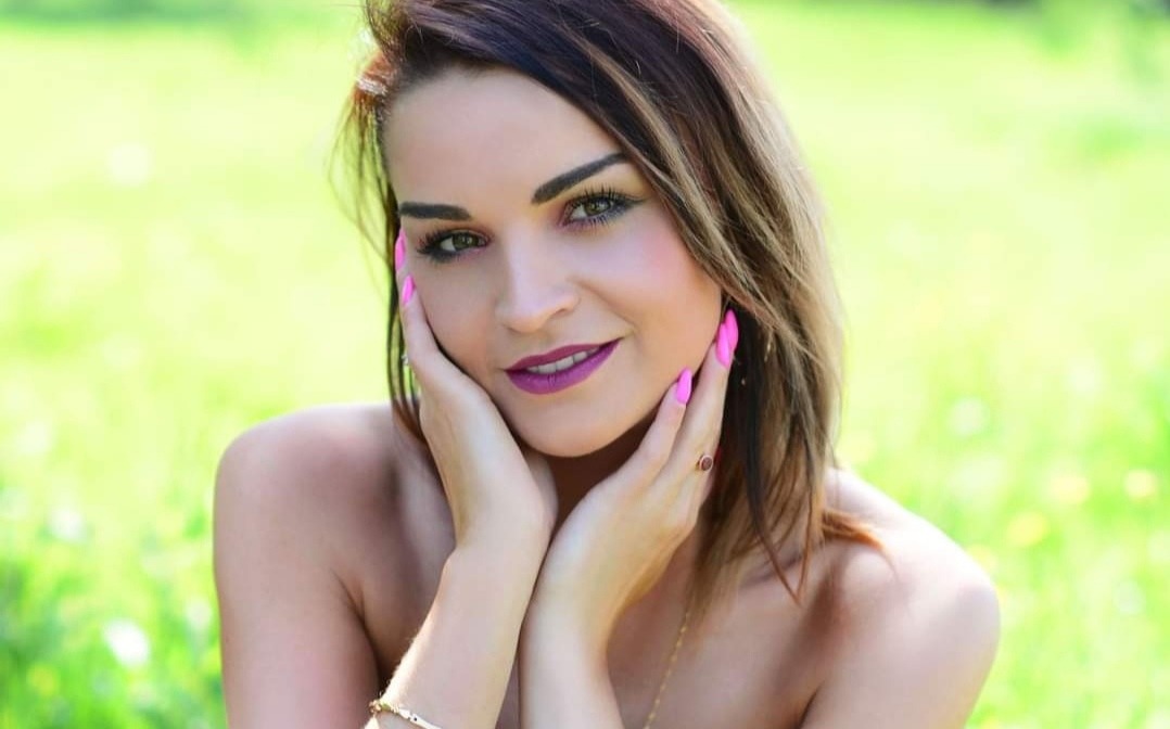 Portret uśmiechniętej kobiety z makijażem i różowymi paznokciami na tle zieleni