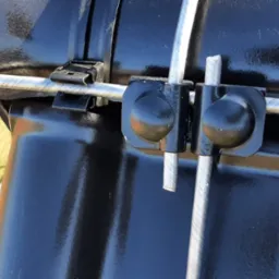 Detale mocowania przewodów odgromowych do czarnej dachówki, widoczne uchwyty i przewody z bliska.