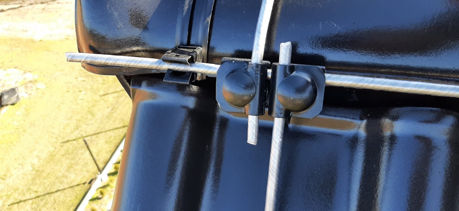 Detale mocowania przewodów odgromowych do czarnej dachówki, widoczne uchwyty i przewody z bliska.