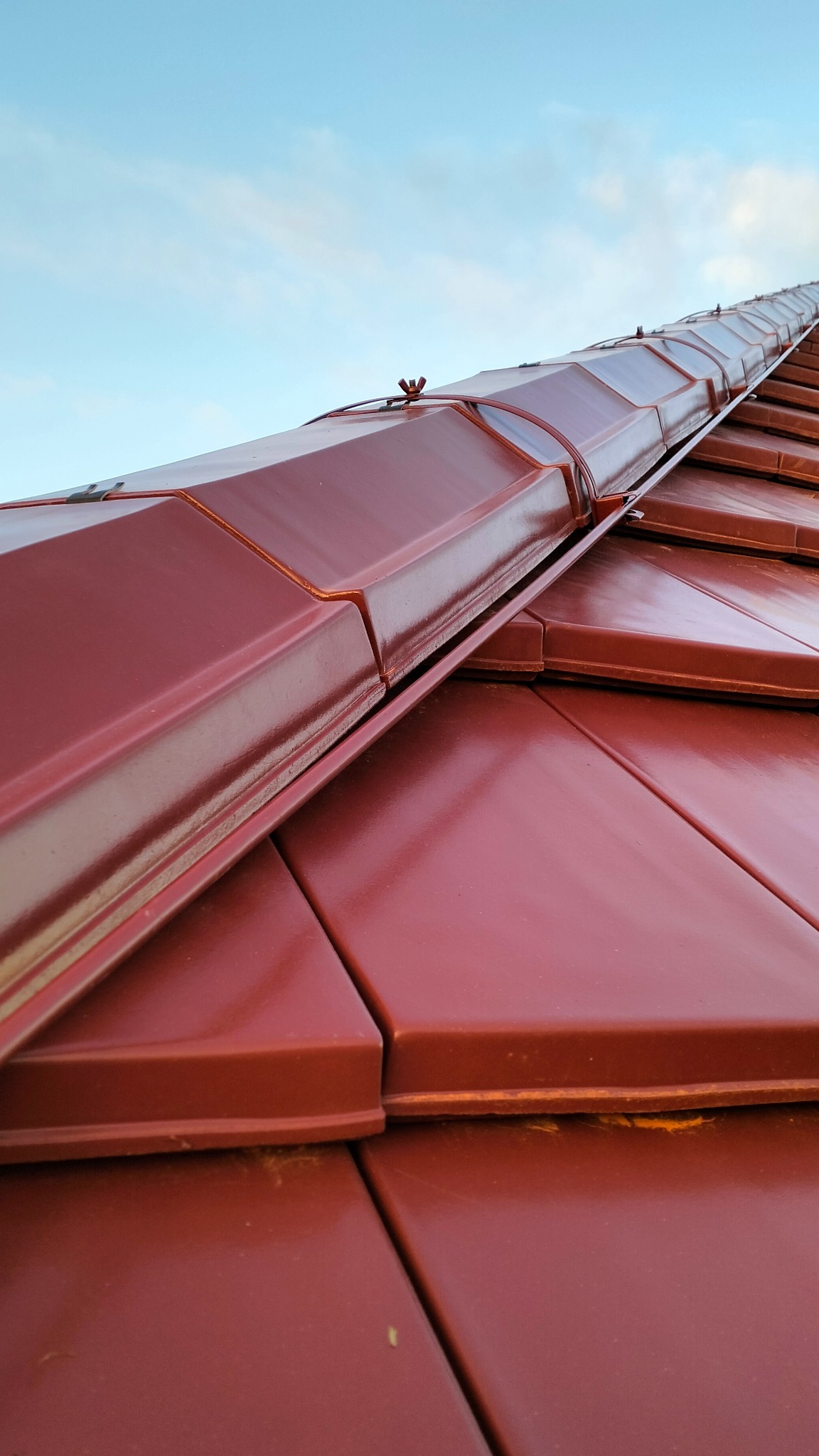 Czerwona dachówka ceramiczna z widocznymi mocowaniami odgromowymi na tle błękitnego nieba.