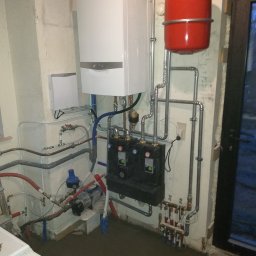 Robert Kulesza - Instalacja centralnego ogrzewania: biały piec gazowy Vaillant, czerwony zbiornik wyrównawczy, czarna skrzynka rozdzielacza z zielonymi diodami, liczne rury miedziane i stalowe, pompa obiegowa...