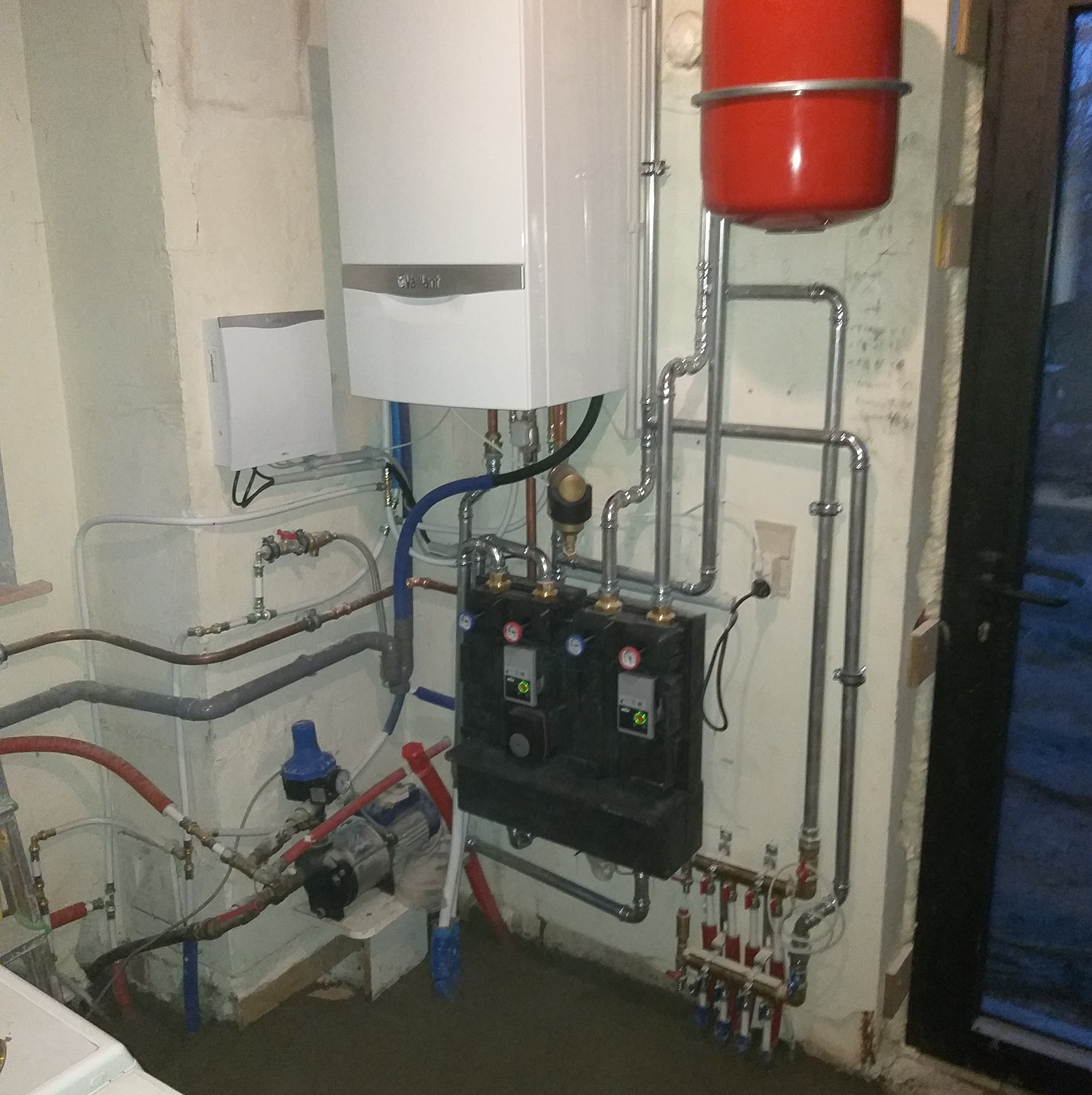 Instalacja centralnego ogrzewania: biały piec gazowy Vaillant, czerwony zbiornik wyrównawczy, czarna skrzynka rozdzielacza z zielonymi diodami, liczne rury miedziane i stalowe, pompa obiegowa...