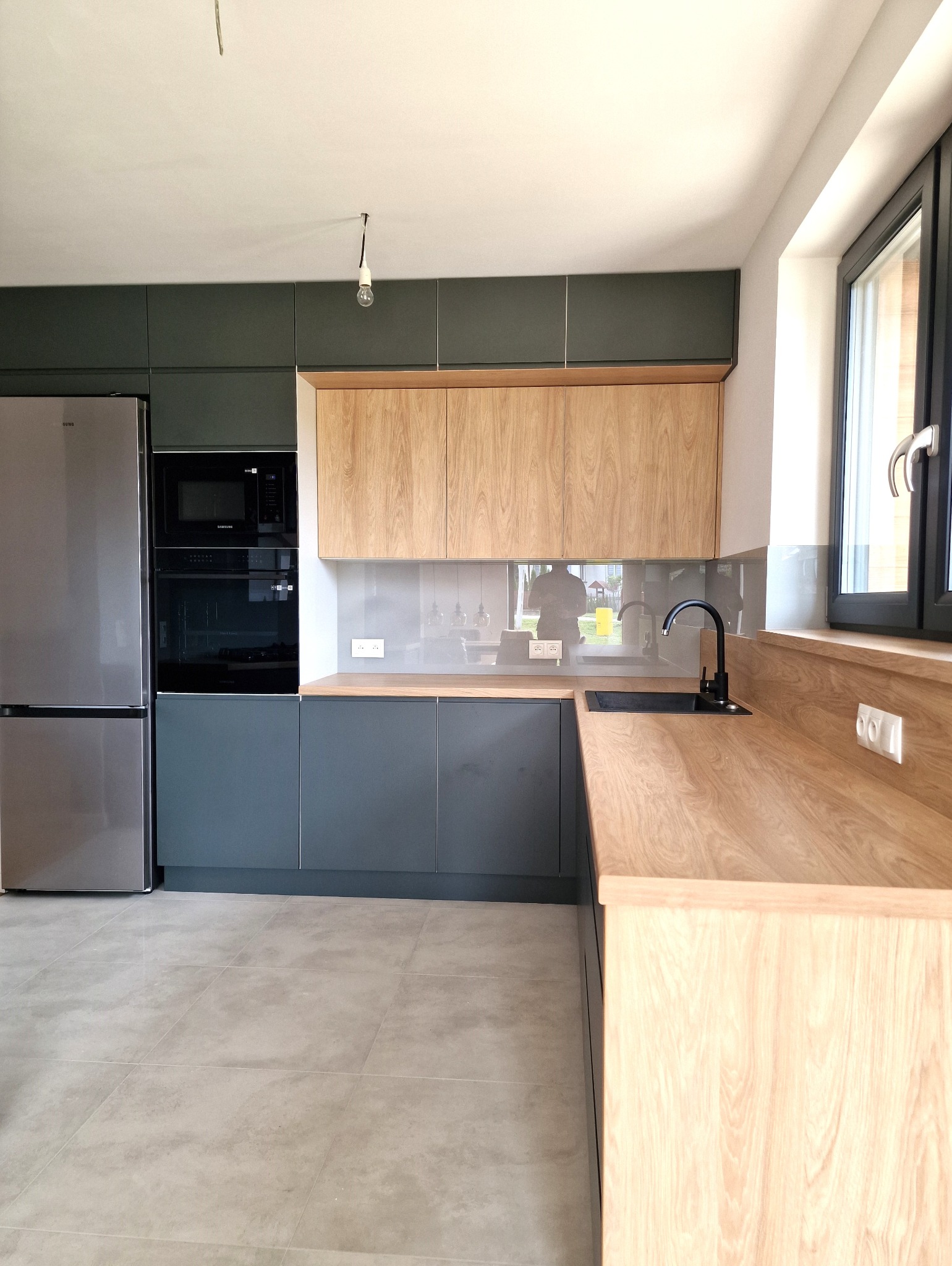 Kuchnia z frontami lakierowanymi i uchwytem frezowanym RAL 7043, blat, elementy w kolorze drewna: Dąb Hikora