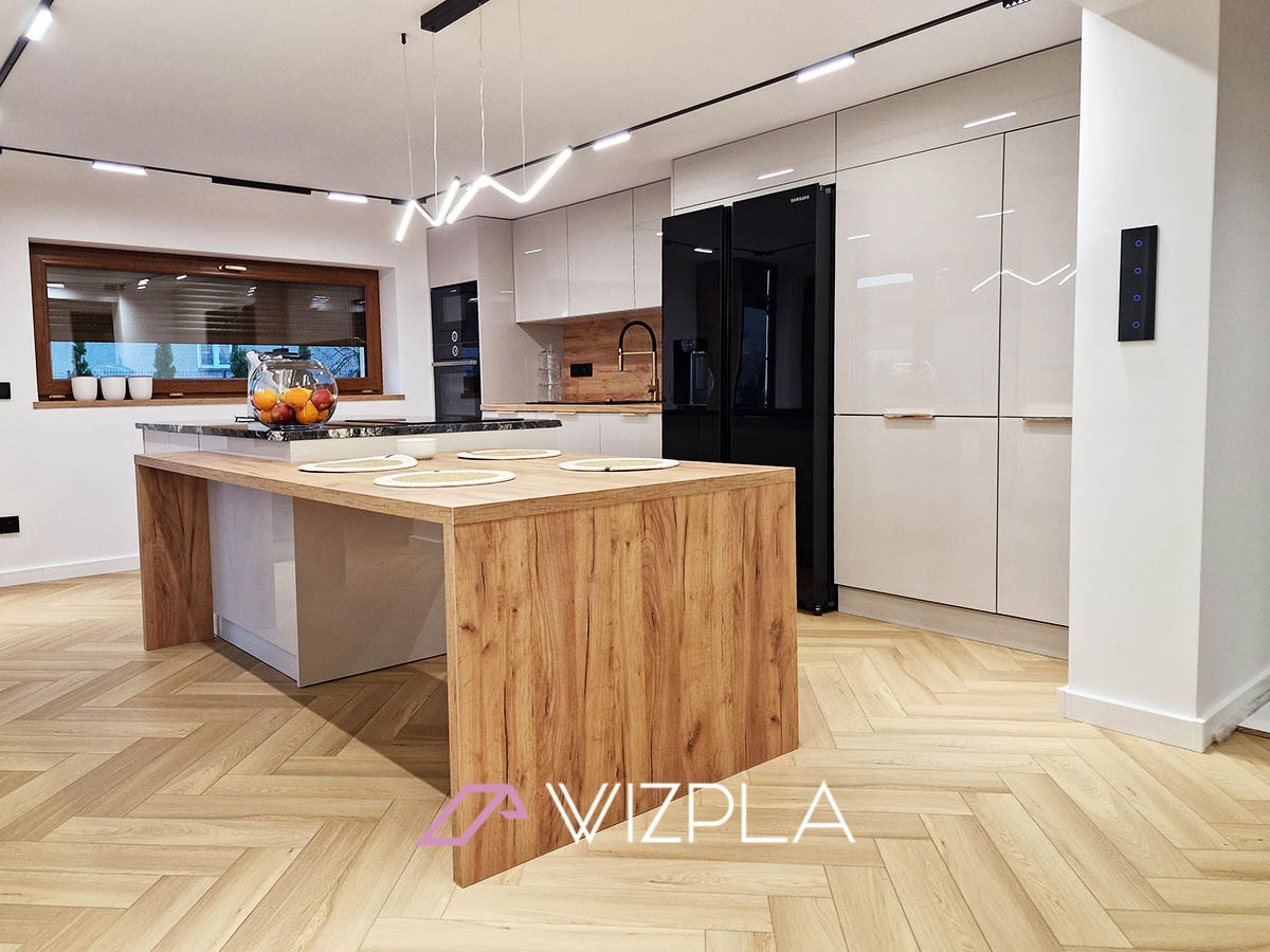 Nowoczesna kuchnia z wyspą o drewnianym wykończeniu, białe lakierowane szafki, czarna lodówka Samsung, parkiet w jodełkę.