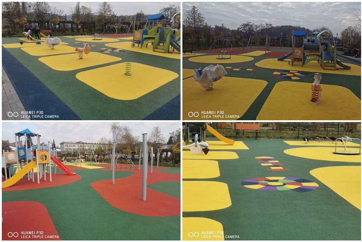 Kolorowy plac zabaw z nawierzchnią z granulatu gumowego w odcieniach zieleni, żółci, czerwieni i niebieskiego, z różnymi urządzeniami do zabawy, w tym huśtawkami sprężynowymi, zjeżdżalniami...