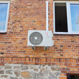 Moja-klima.pl - Biały klimatyzator Rotenso zamontowany na ceglanej ścianie budynku z kamienną podmurówką, widoczny biały przewód odprowadzający skropliny i okno z białymi ramami.