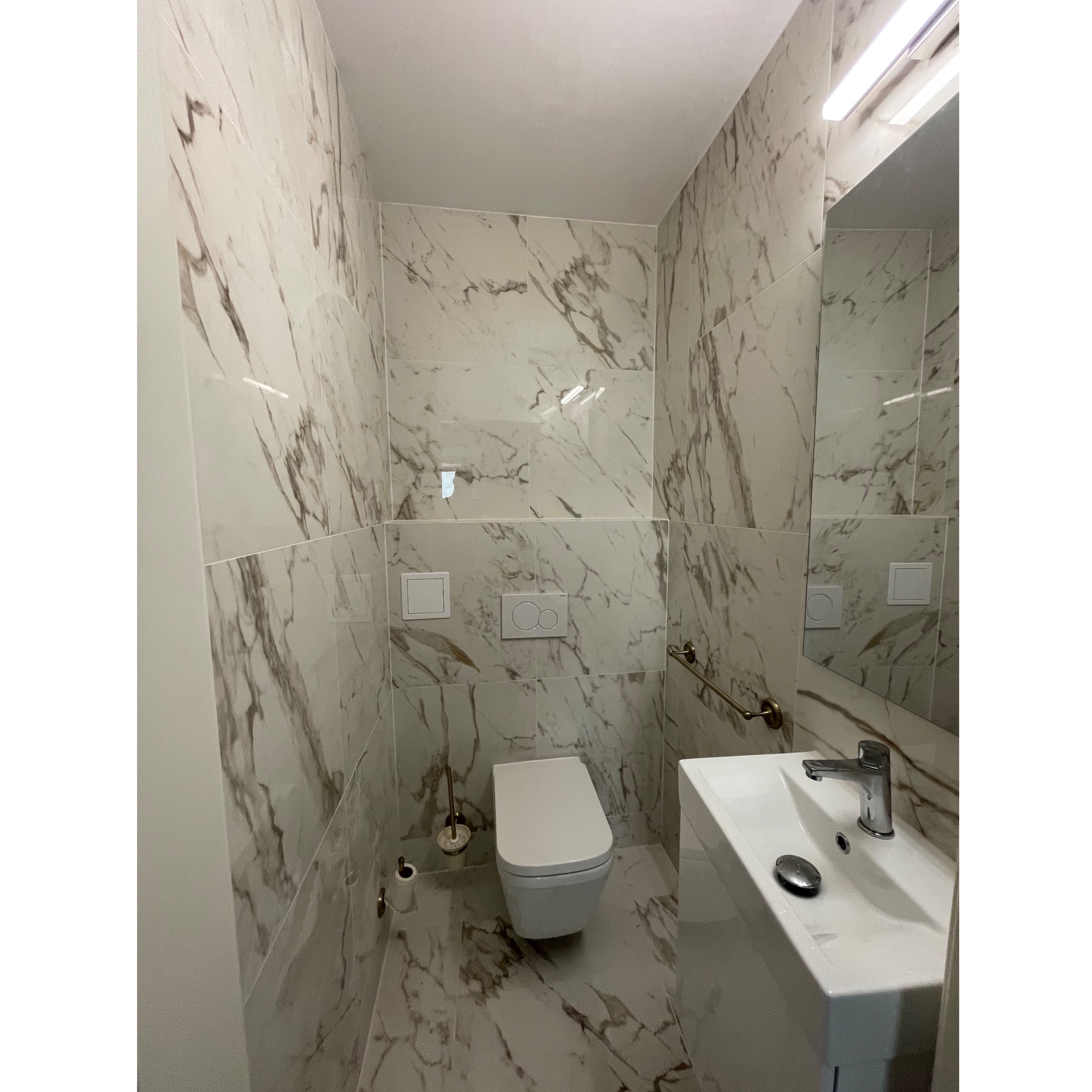 Nowoczesna, mała łazienka z marmurowymi płytkami na ścianach i podłodze, wisząca toaleta, umywalka nablatowa z chromowaną baterią i akcesoria w kolorze starego złota.