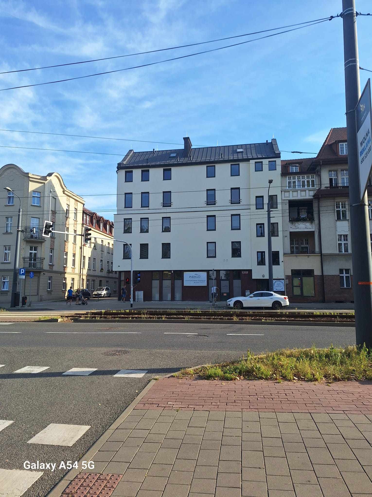 Odnowiona, biała elewacja budynku w Rybniku z ciemnymi ramami okiennymi, widoczna z perspektywy ulicy, z przejeżdżającym białym samochodem.