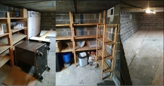 Piwnica z regałami przed opróżnianiem, widoczne drewniane półki, biurko na kółkach i betonowe ściany.