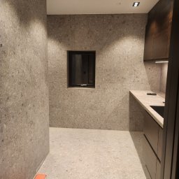 Firma-Remontowo-Budowlana Strzępek Przemysław - Wykończona łazienka z szarymi płytkami imitującymi lastryko na ścianach i podłodze, czarne akcenty w postaci okna i szafek, widoczne kartony z płytkami Casalgrande Padana.