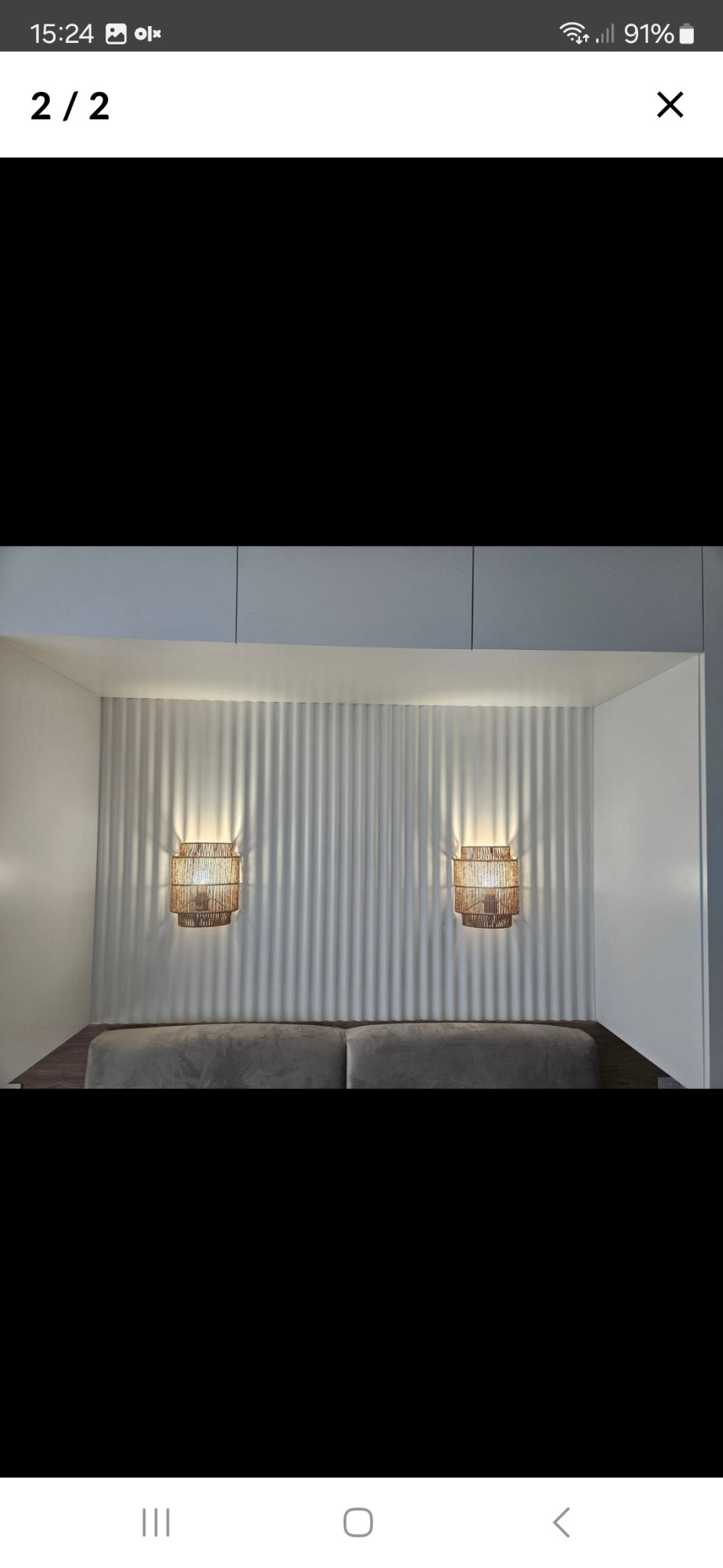 Minimalistyczne wnętrze: sofa z szarego weluru, biała ściana z pionowymi żłobieniami i dwie wiklinowe lampy ścienne. Nowoczesny design, ciepłe światło.