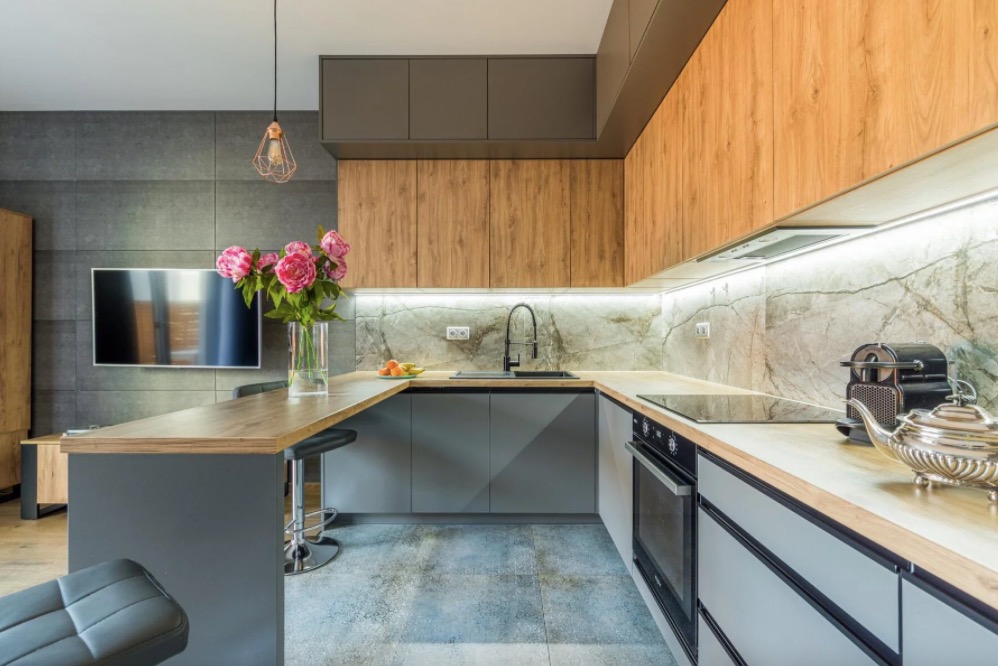 Nowoczesna kuchnia w odcieniach szarości i drewna z wyspą, oświetleniem LED pod szafkami i bukietem różowych piwonii w wazonie na blacie.