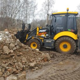 Rateko Robert Szczurowski - Żółto-czarna koparko-ładowarka MST w błotnistym terenie, pracująca przy pryzmie gruzu i ziemi, z widocznym numerem telefonu na kabinie i drzewami w tle.