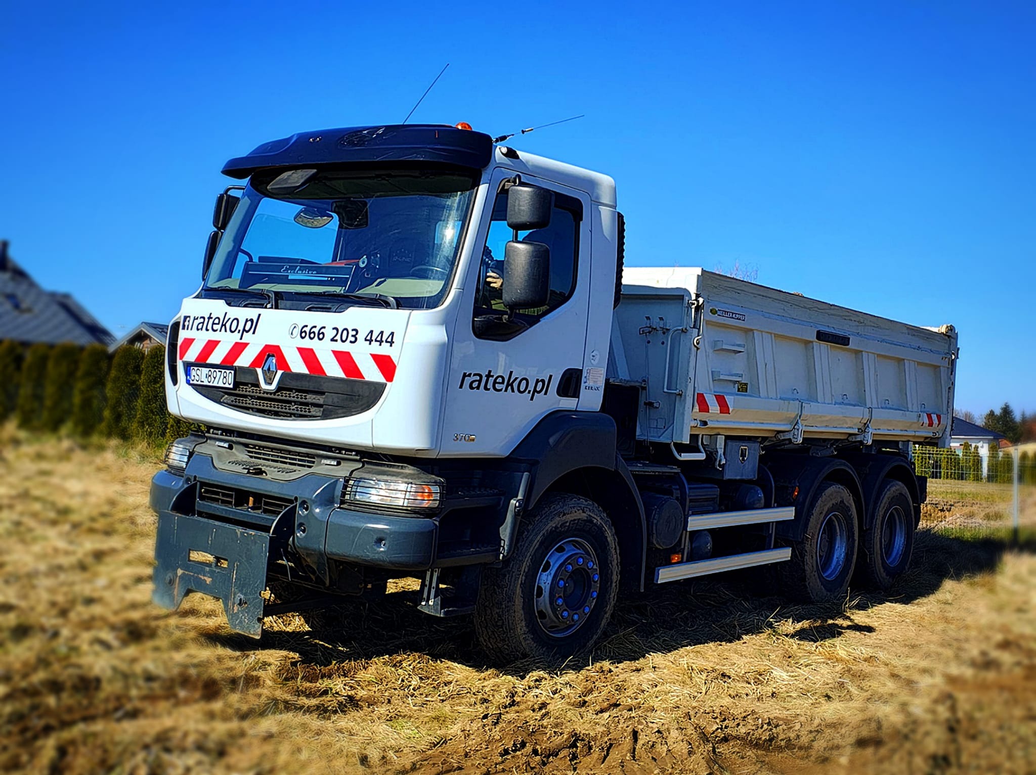 Ciężarówka wywrotka Renault z logo firmy Rateko.pl na tle błękitnego nieba i pola. Widoczne numery kontaktowe i tablica rejestracyjna GSL-89780.