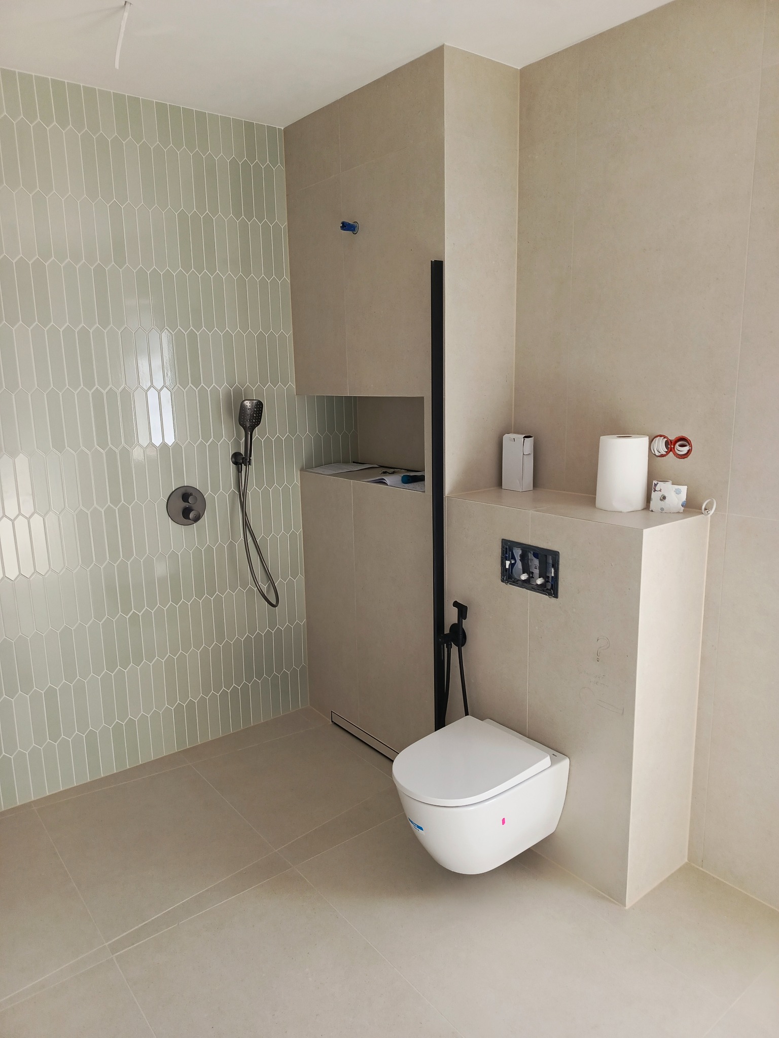 Wykończona łazienka w beżach i szarościach z podwieszaną toaletą, armaturą w kolorze czarnym i nietypowymi płytkami w strefie prysznica.