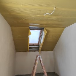 Konrad Ciepliński - Poddasze z oknem dachowym w trakcie prac wykończeniowych. Widoczna folia paroizolacyjna na suficie i ściany przygotowane do dalszych prac. Stoi drabina.