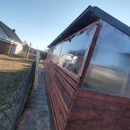 Konrad Ciepliński - Drewniana altana z przezroczystymi panelami, widok z boku na tle błękitnego nieba. Na ziemi leży pomarańczowy przedłużacz, obok ogrodzenie i elementy konstrukcyjne.