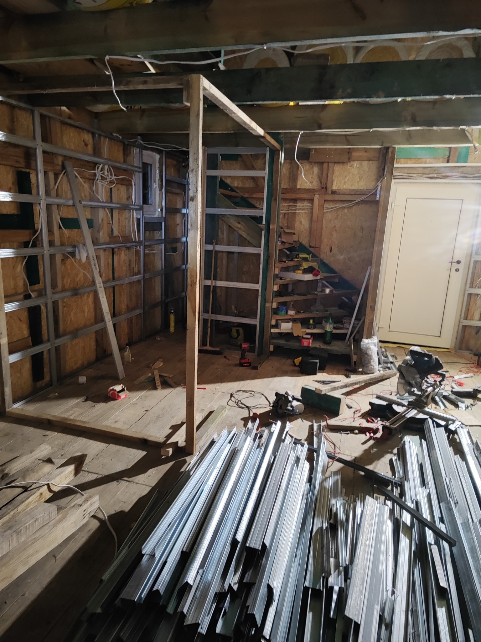 Konstrukcja szkieletowa z profili metalowych w surowym wnętrzu. Widoczne narzędzia i materiały budowlane. Etap prac przygotowawczych do wykończenia ścian.