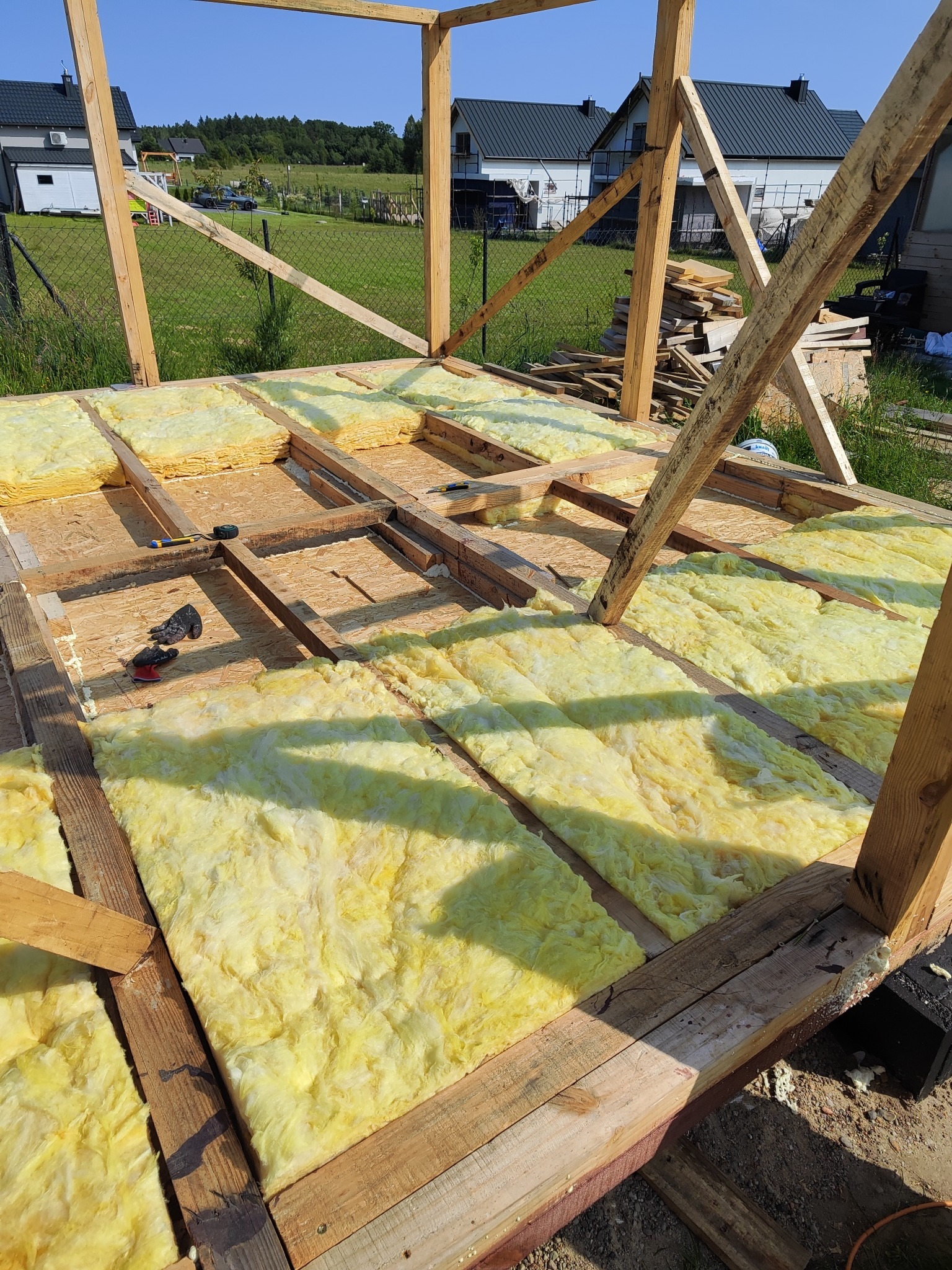 Ocieplenie podłogi wełną mineralną w drewnianej konstrukcji szkieletowej domu jednorodzinnego w trakcie budowy. Widoczne narzędzia i materiały budowlane.