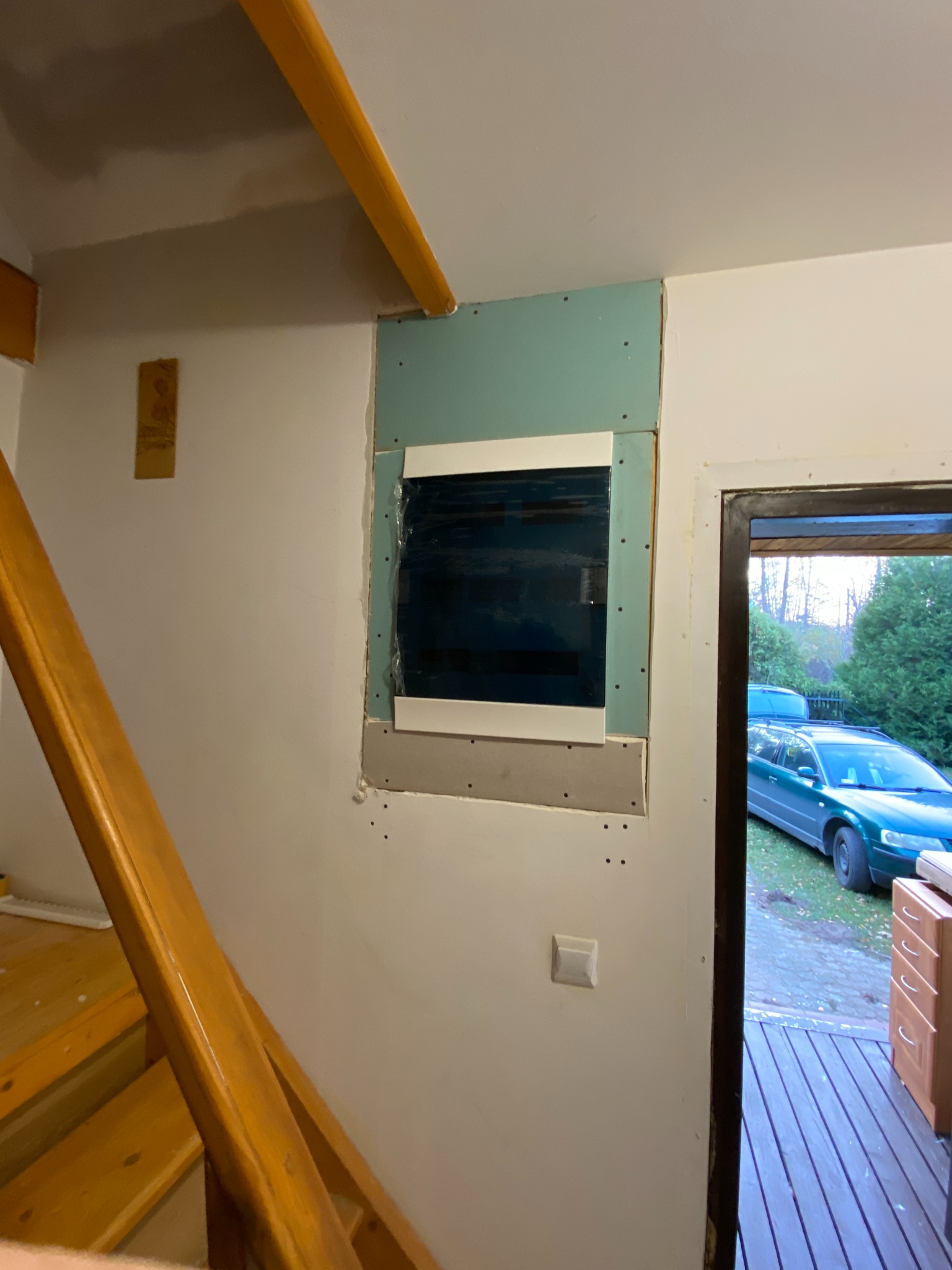 Wnęka na rozdzielnicę elektryczną w trakcie zabudowy płytą gipsową, widoczny fragment schodów i wyłącznik. Prace wykończeniowe wewnątrz budynku.