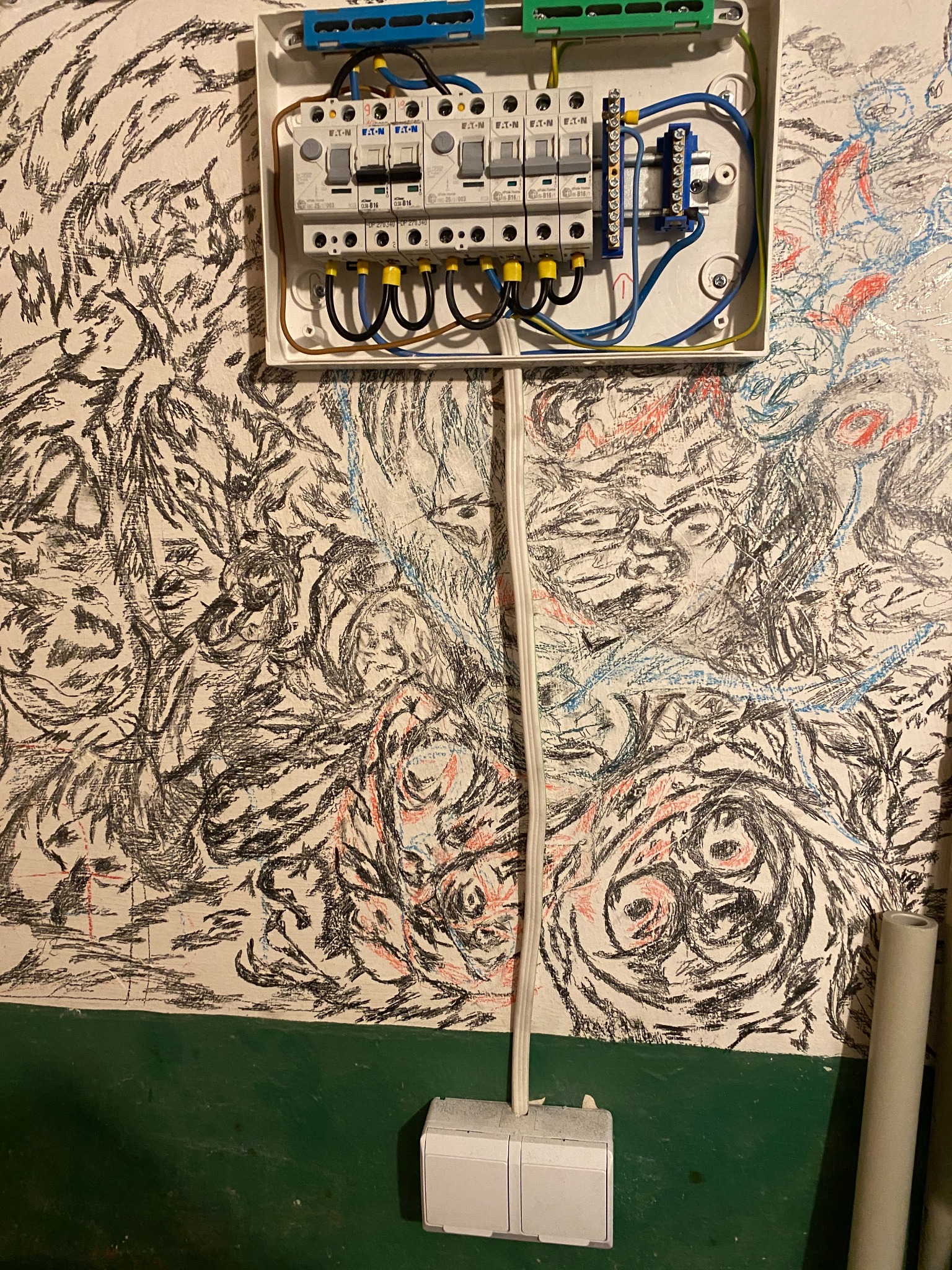 Rozdzielnica elektryczna Eaton z bezpiecznikami na ścianie pokrytej abstrakcyjnymi rysunkami. Widoczny kabel i włącznik światła. Nietypowe tło.