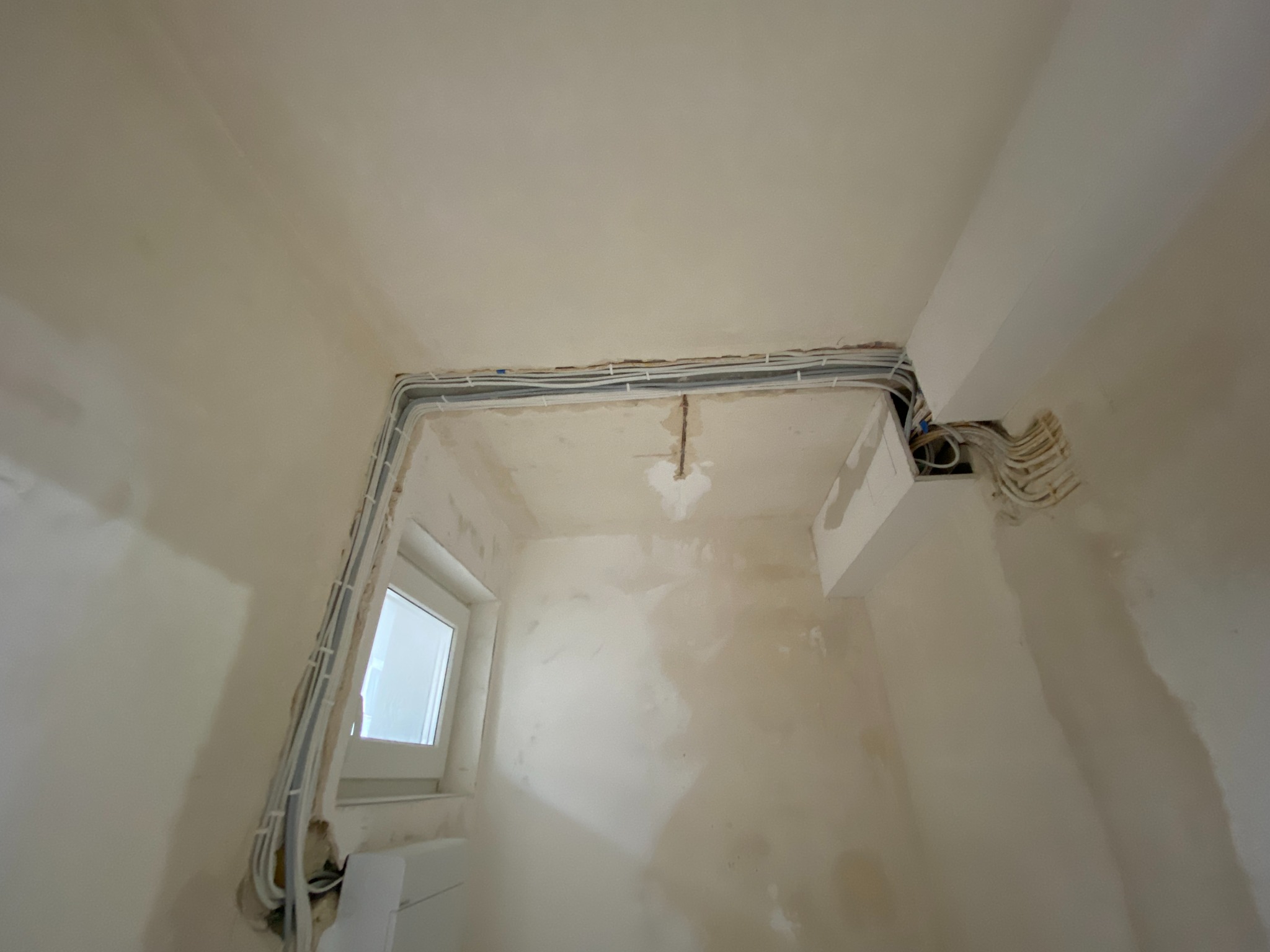 Wnętrze w trakcie prac: kable elektryczne prowadzone wzdłuż ściany przy oknie i pod sufitem. Widoczne niedoskonałości ścian przed wykończeniem.