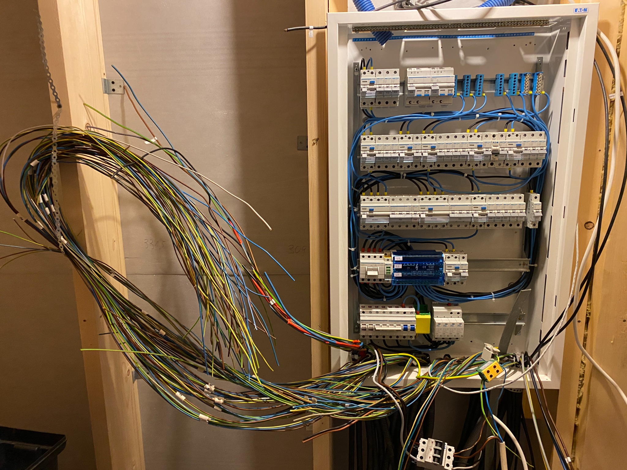 Rozdzielnica elektryczna w trakcie montażu: widoczne kable oznaczone numerami, zabezpieczenia i elementy instalacji w skrzynce. Prace w toku, surowy stan wykończenia.