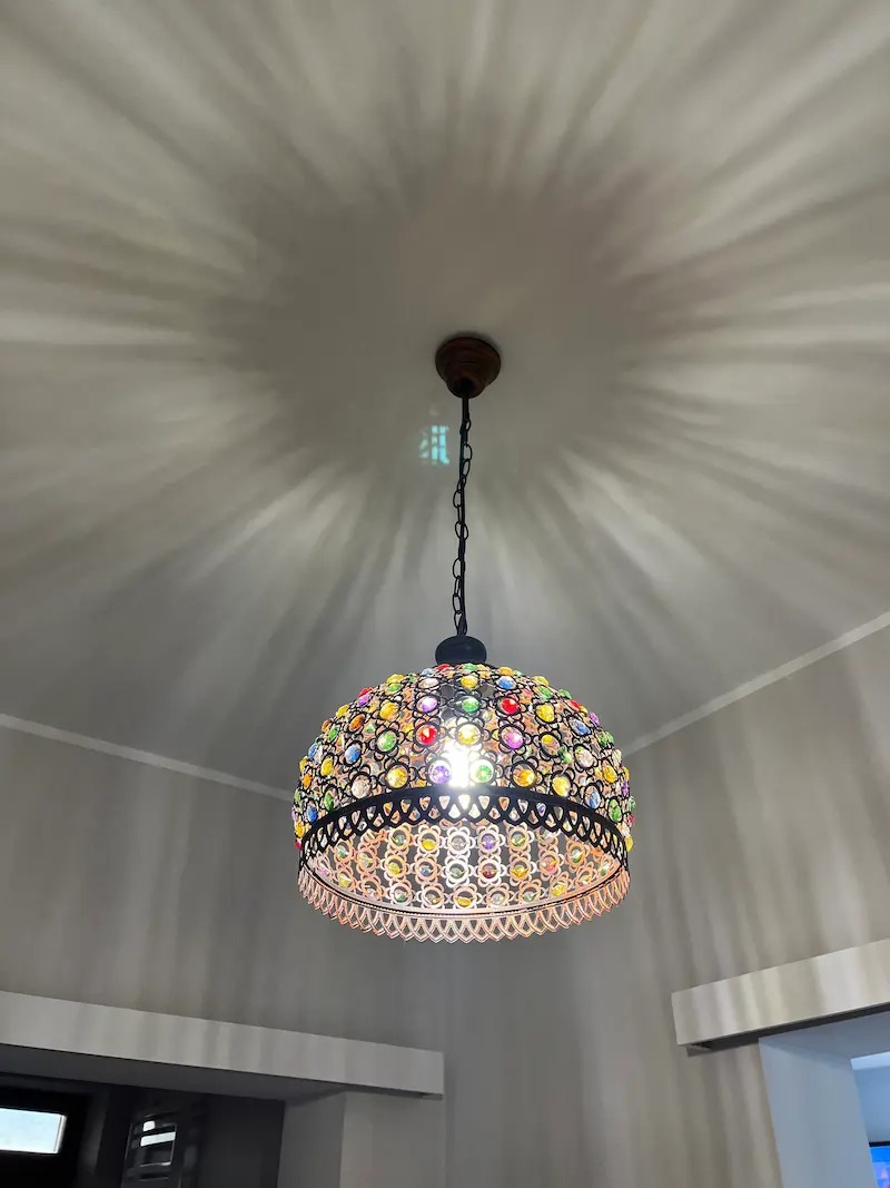 Kolorowa lampa wisząca z kryształkami, oświetlająca sufit wzorem promieni. Dekoracyjne oświetlenie wnętrza, widok od dołu.