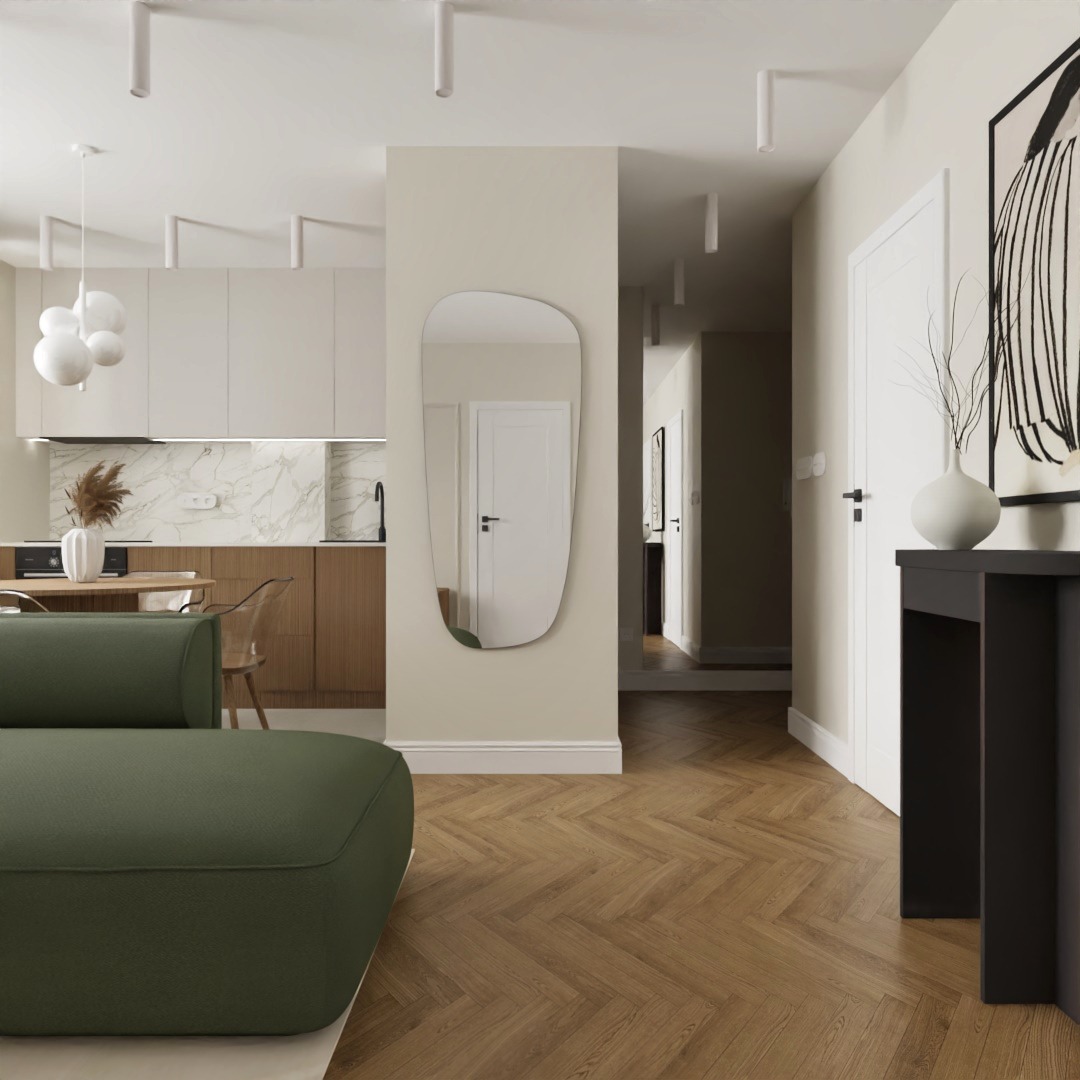 Nowoczesne wnętrze mieszkania z parkietem w jodełkę, zieloną sofą, lustrem o nieregularnym kształcie i widokiem na kuchnię z marmurowym backsplashiem.