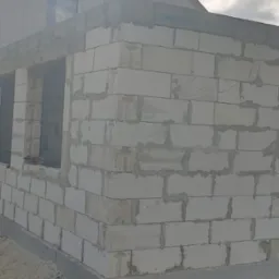 Budowa ściany zewnętrznej z białych bloczków, widoczny fragment budynku z oknem i klimatyzatorem, etap murowania.